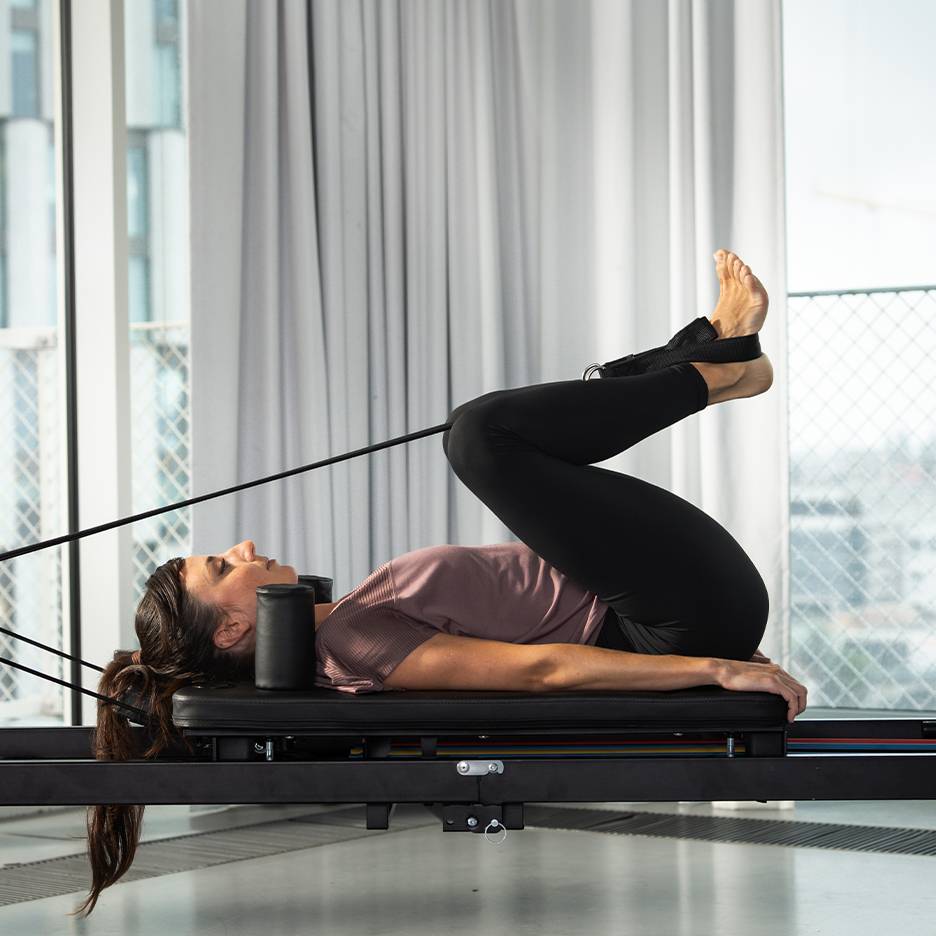 Žena cvičící Pilates na reformer stroji s nohama nahoře.