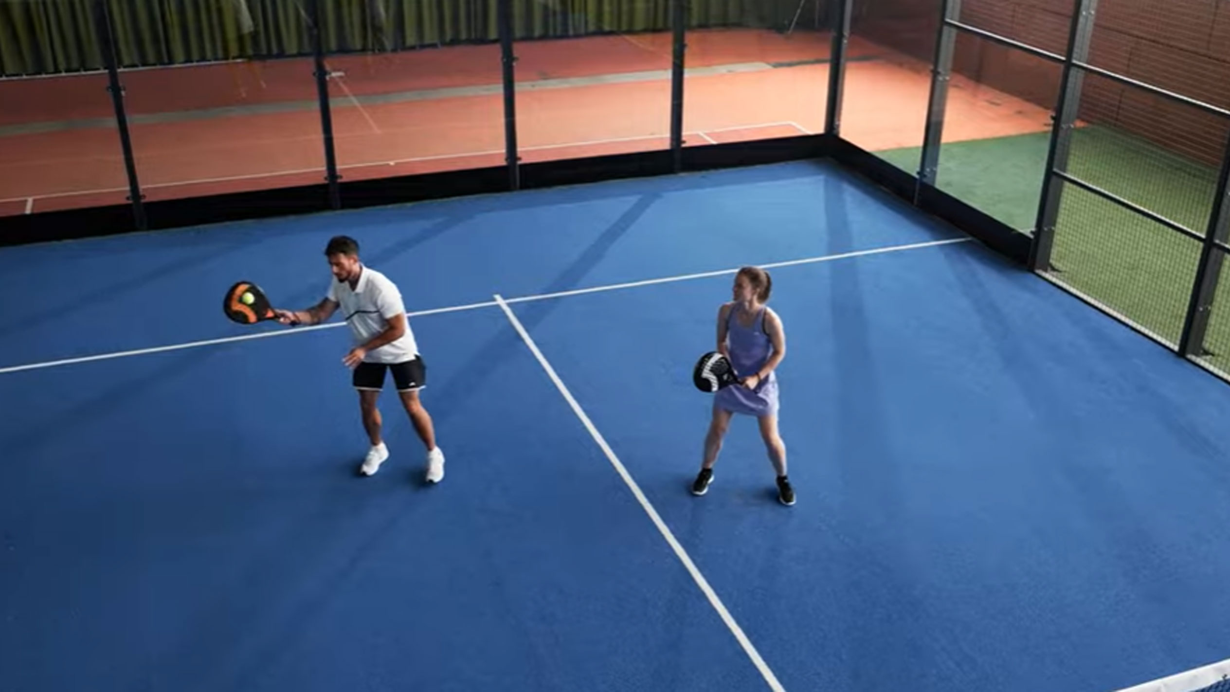 Muž a žena hrají padel na modrém kurtu s pálkami a míčkem