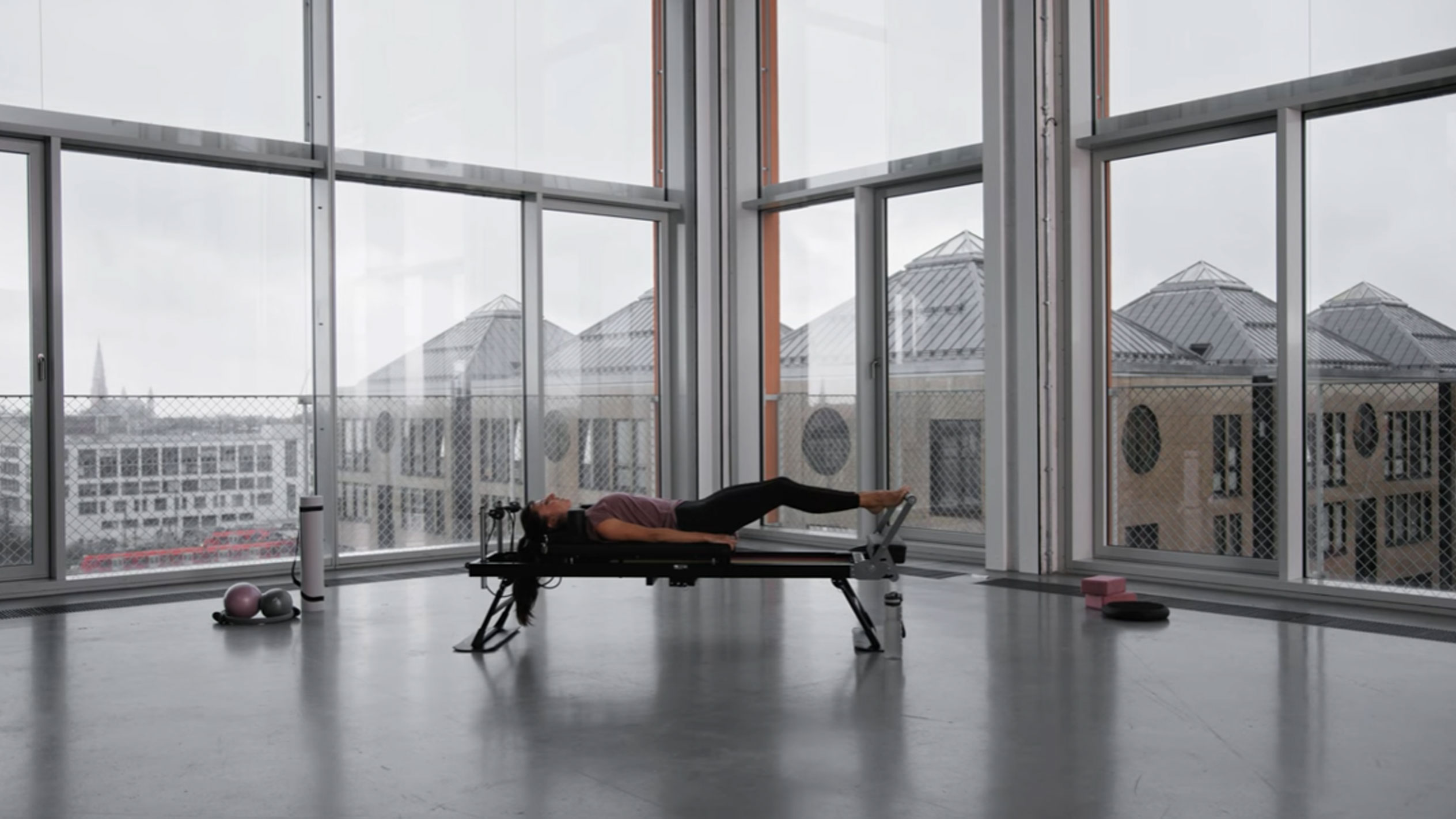 Žena cvičící pilates v moderním studiu s výhledem na město.