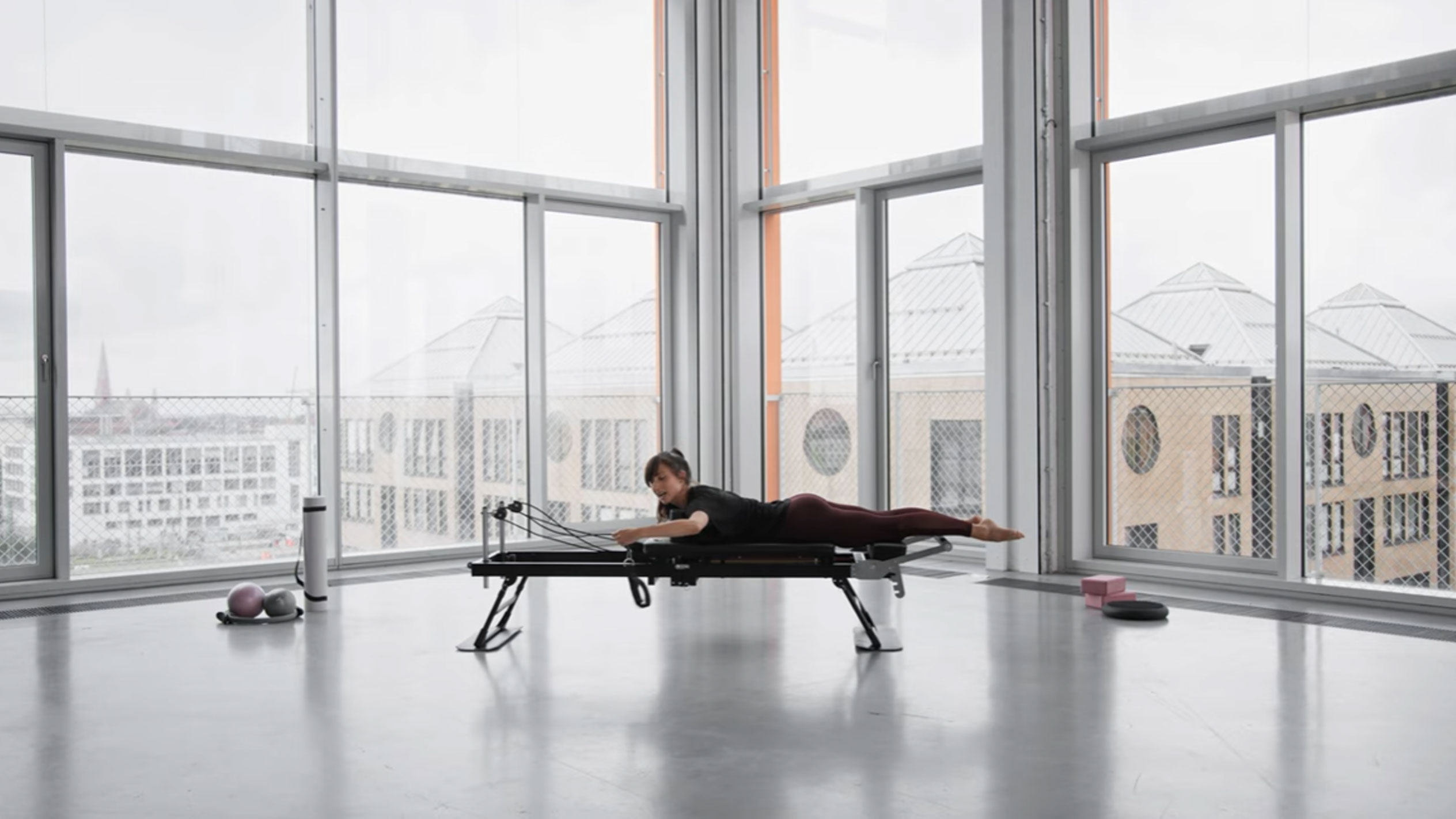 Žena cvičící pilates na reformeru s výhledem na město.