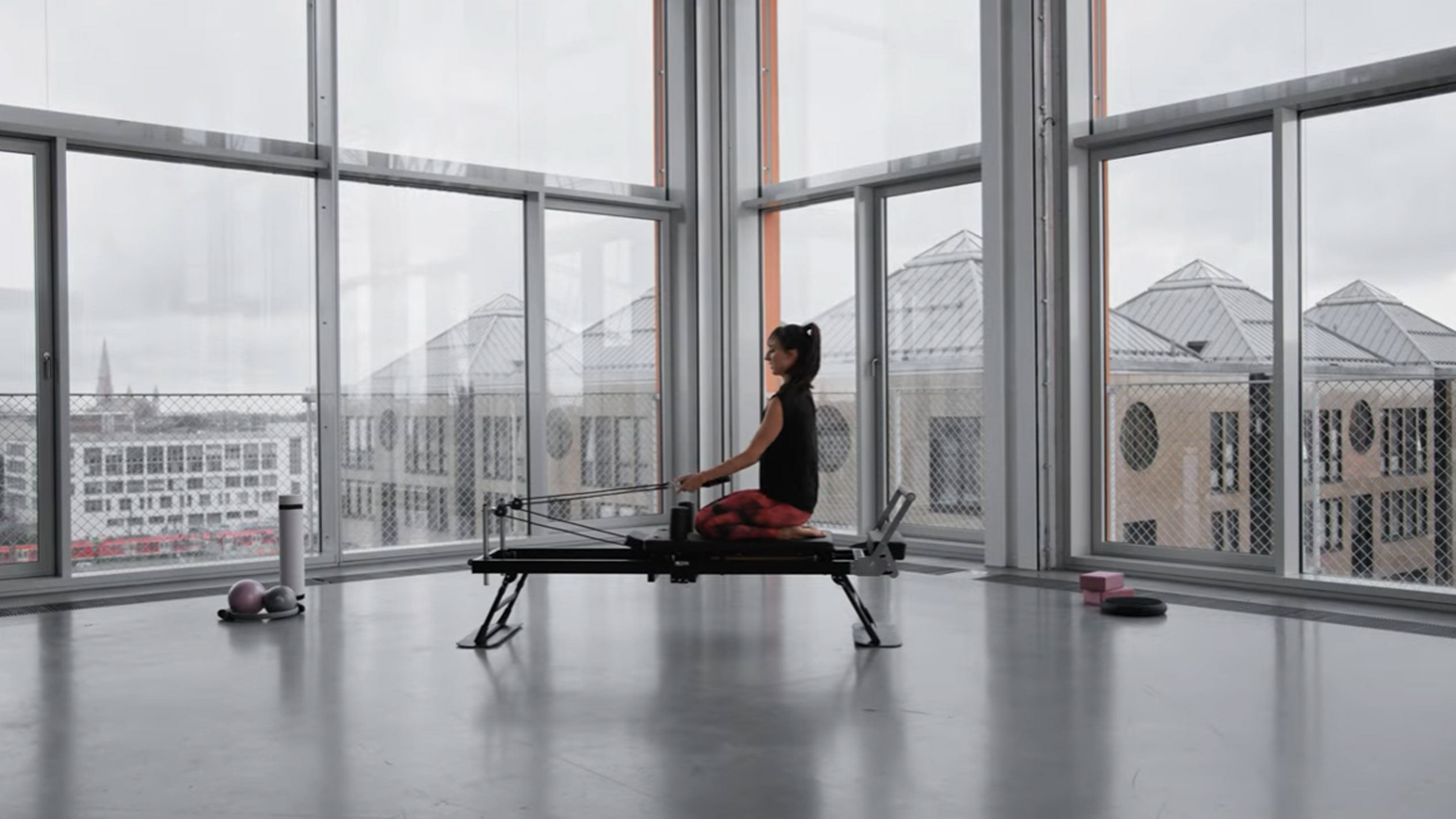 Žena cvičící pilates na reformeru s výhledem na město.
