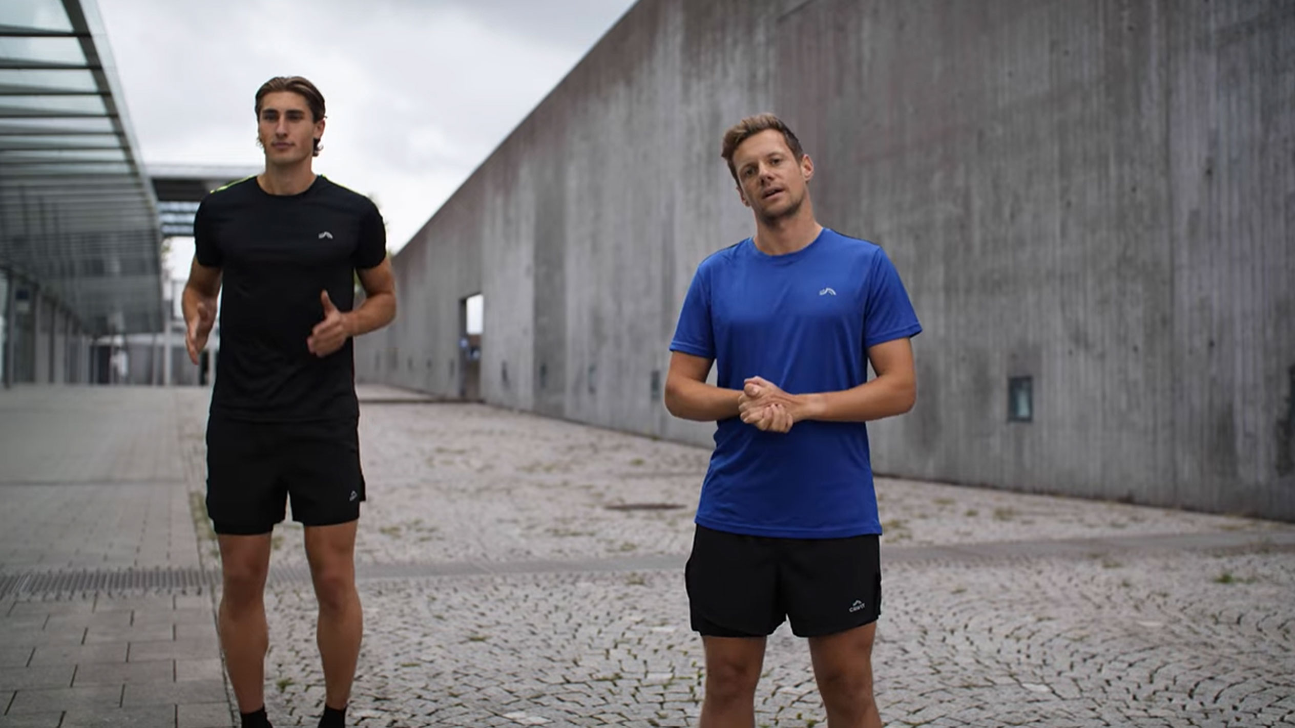 Dva muži v černém a modrém sportovním oblečení venku.