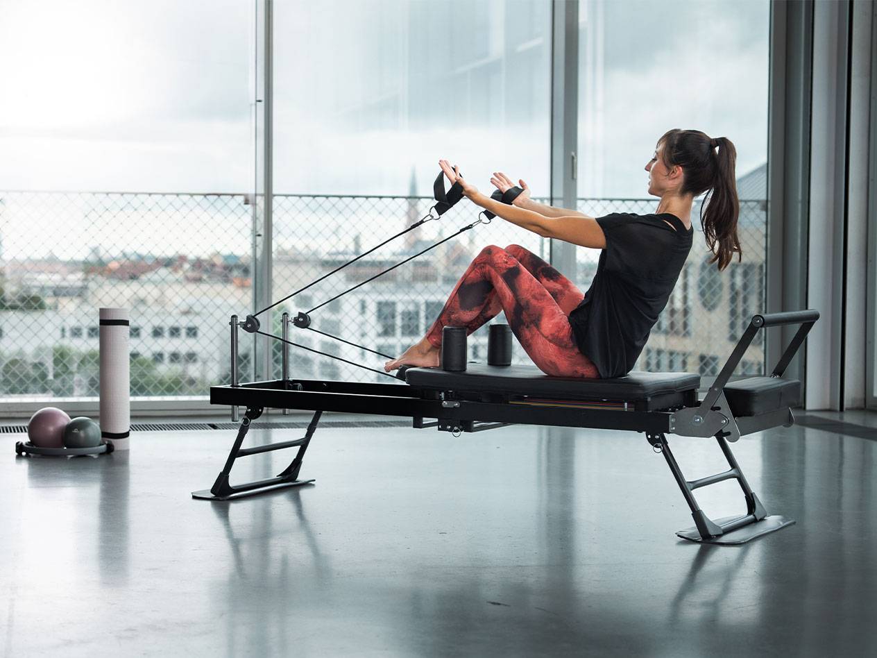 Žena cvičící pilates na reformer stroji s výhledem na město.