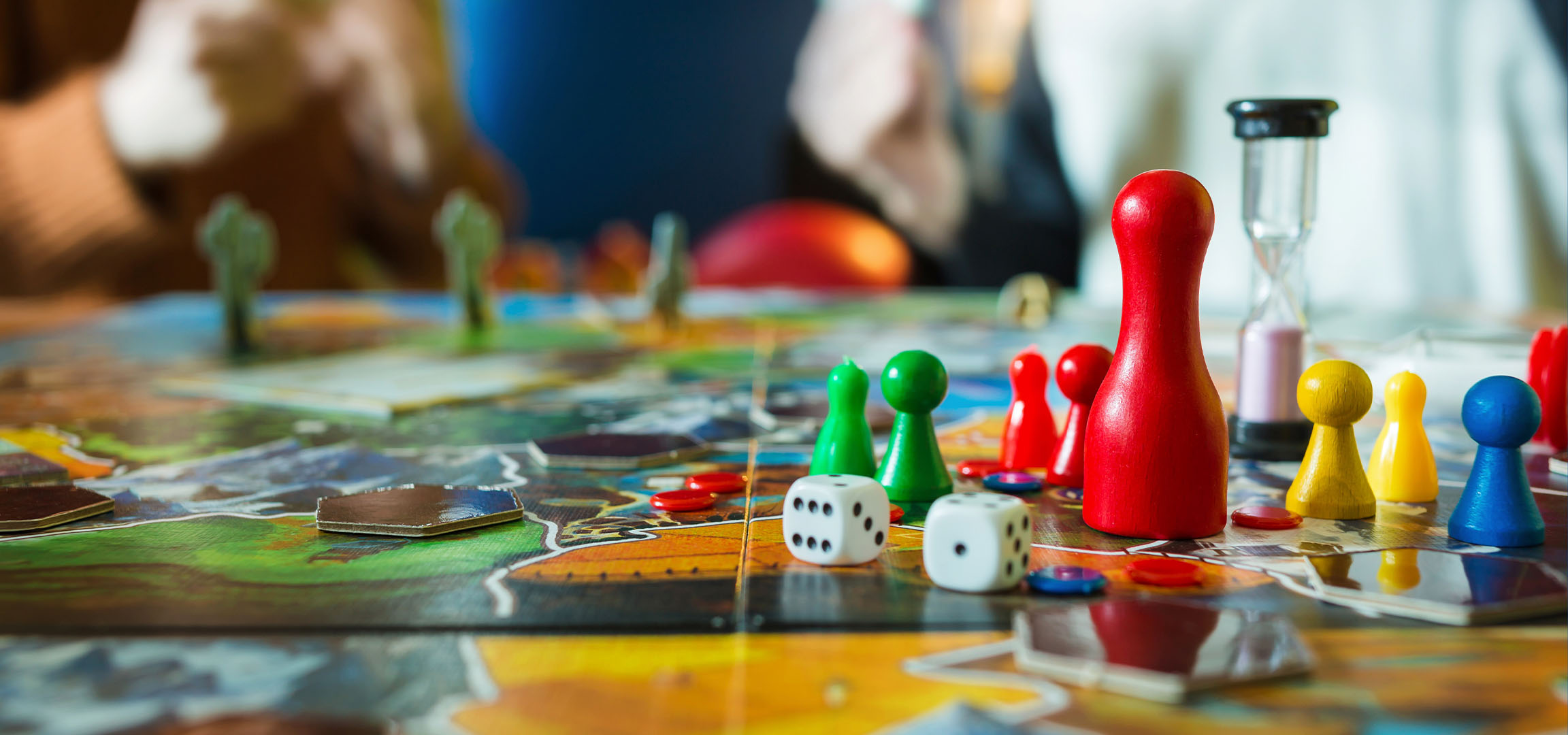 Barevné figurky deskové hry, včetně červených, zelených, žlutých a modrých pěšců, s kostkami.