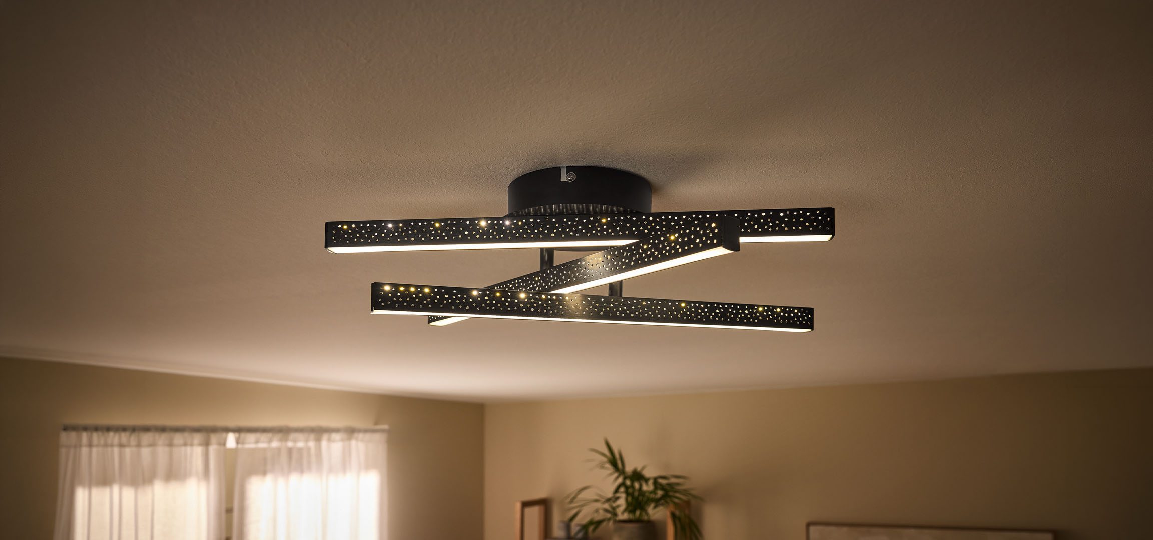 Moderní LED stropní svítidlo s černými, perforovanými tyčemi a teplým světlem.