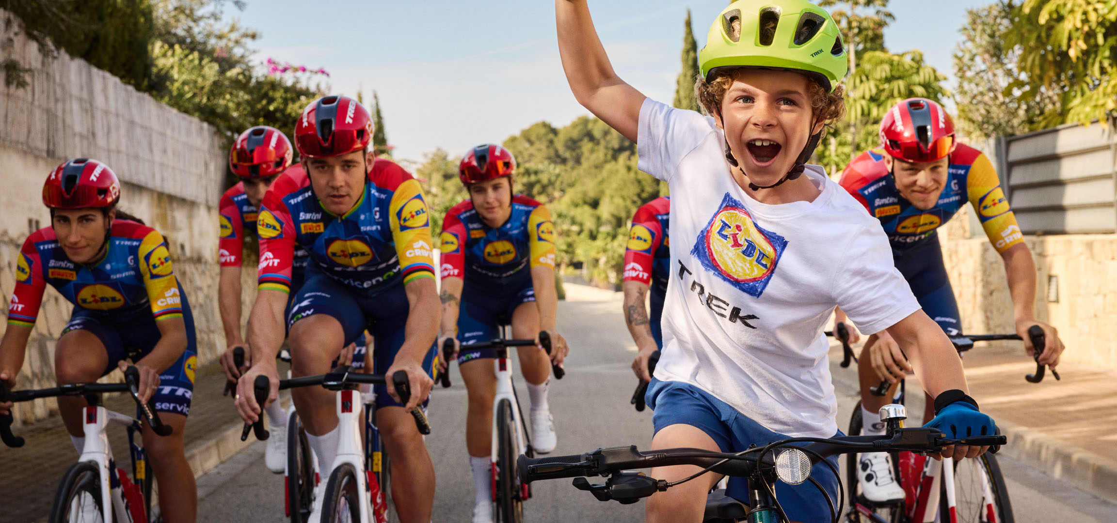 Dítě v přilbě a tričku s logem Lidl, obklopené cyklisty.