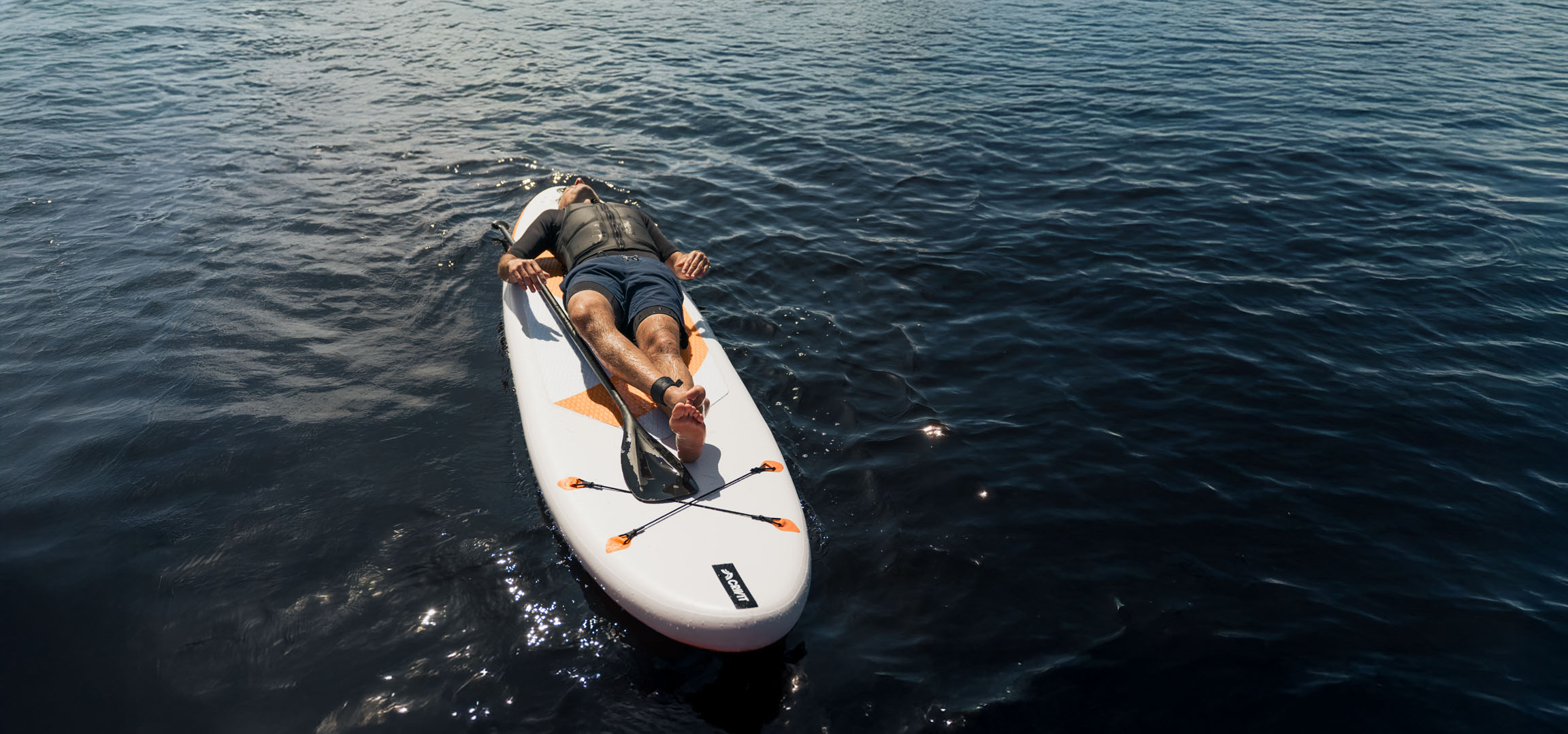 Muž relaxuje na paddleboardu v klidné vodě.