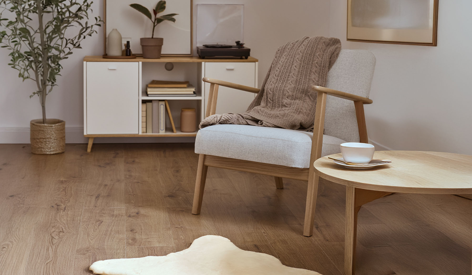 Pohodlné křeslo s dekou, dřevěný konferenční stolek a úložná skříňka ve světlém obývacím pokoji.