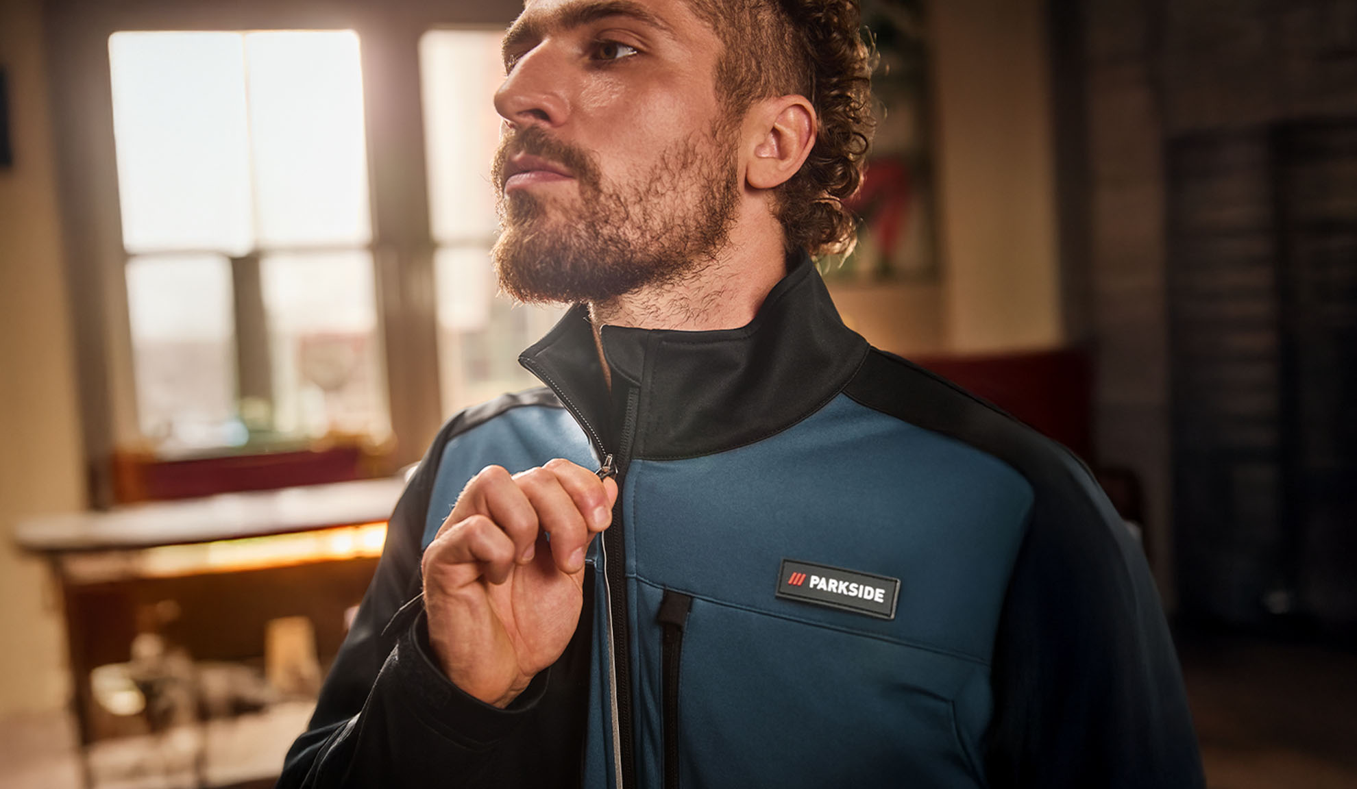 Muž v modro-černé pracovní bundě Parkside, zapínající si ji.