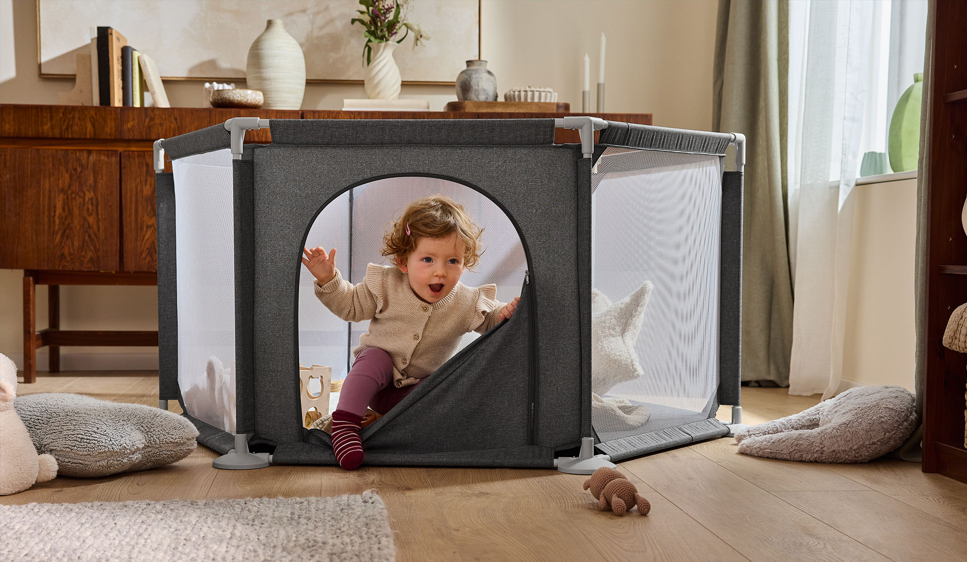 Šťastné dítě vylézá z šedé ohrádky v útulném obývacím pokoji.