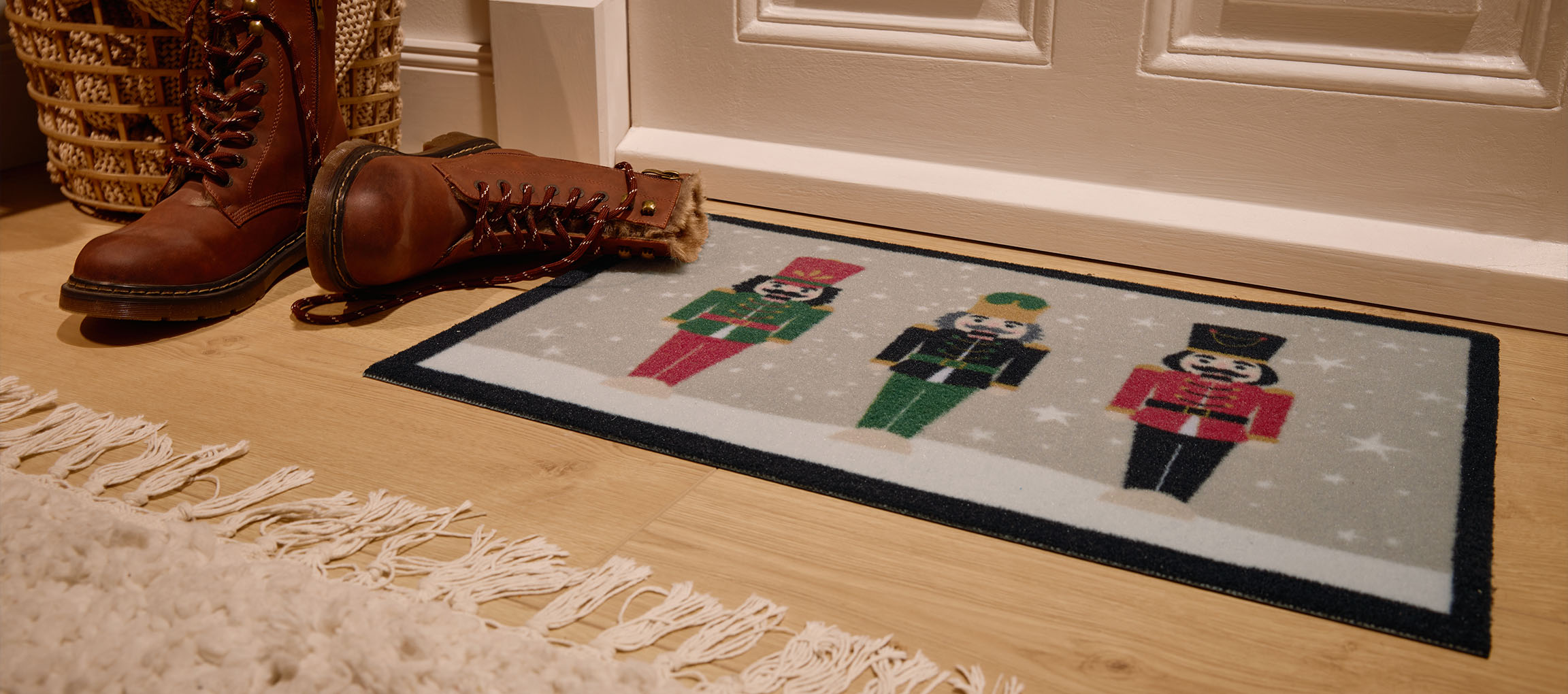 Vánoční rohožka s louskáčky, hnědé boty a proutěný koš u vchodu.