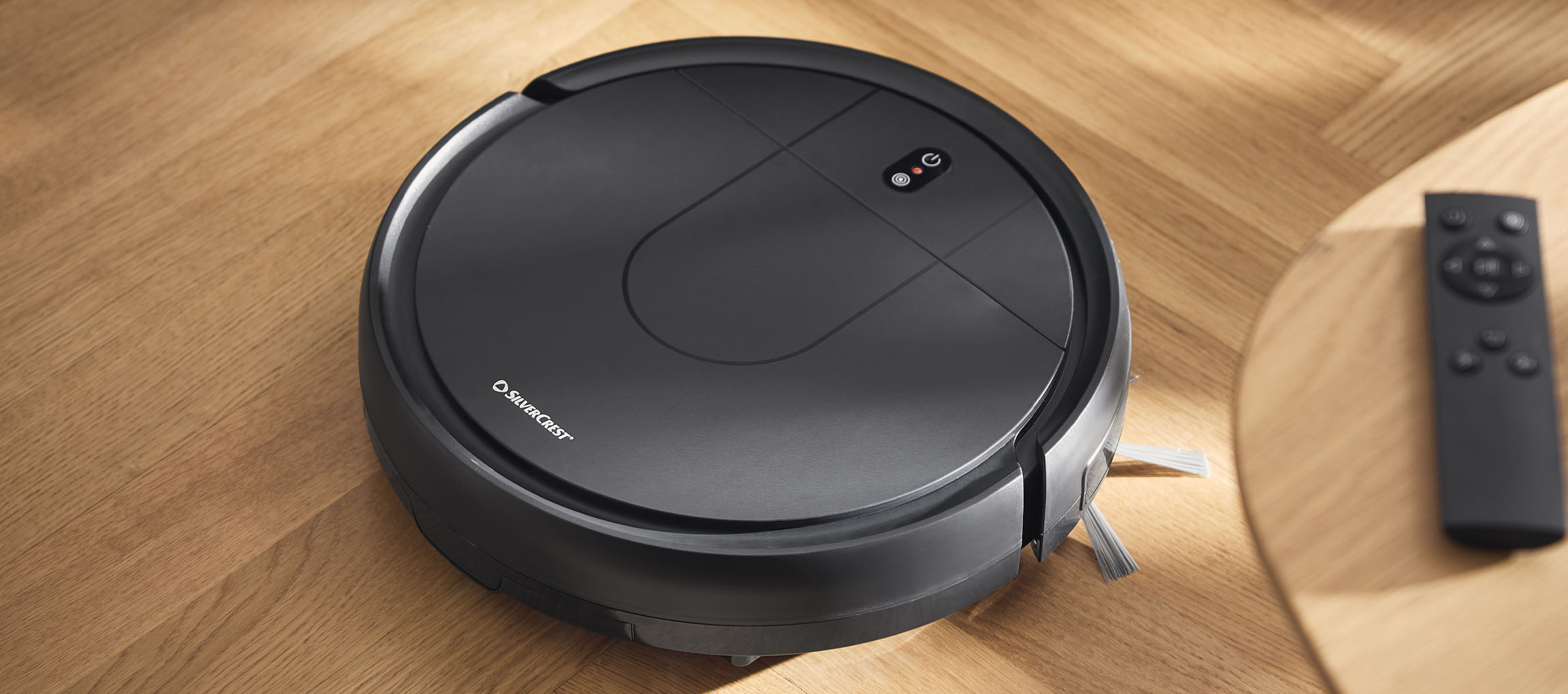 Černý robotický vysavač na dřevěné podlaze s dálkovým ovládáním