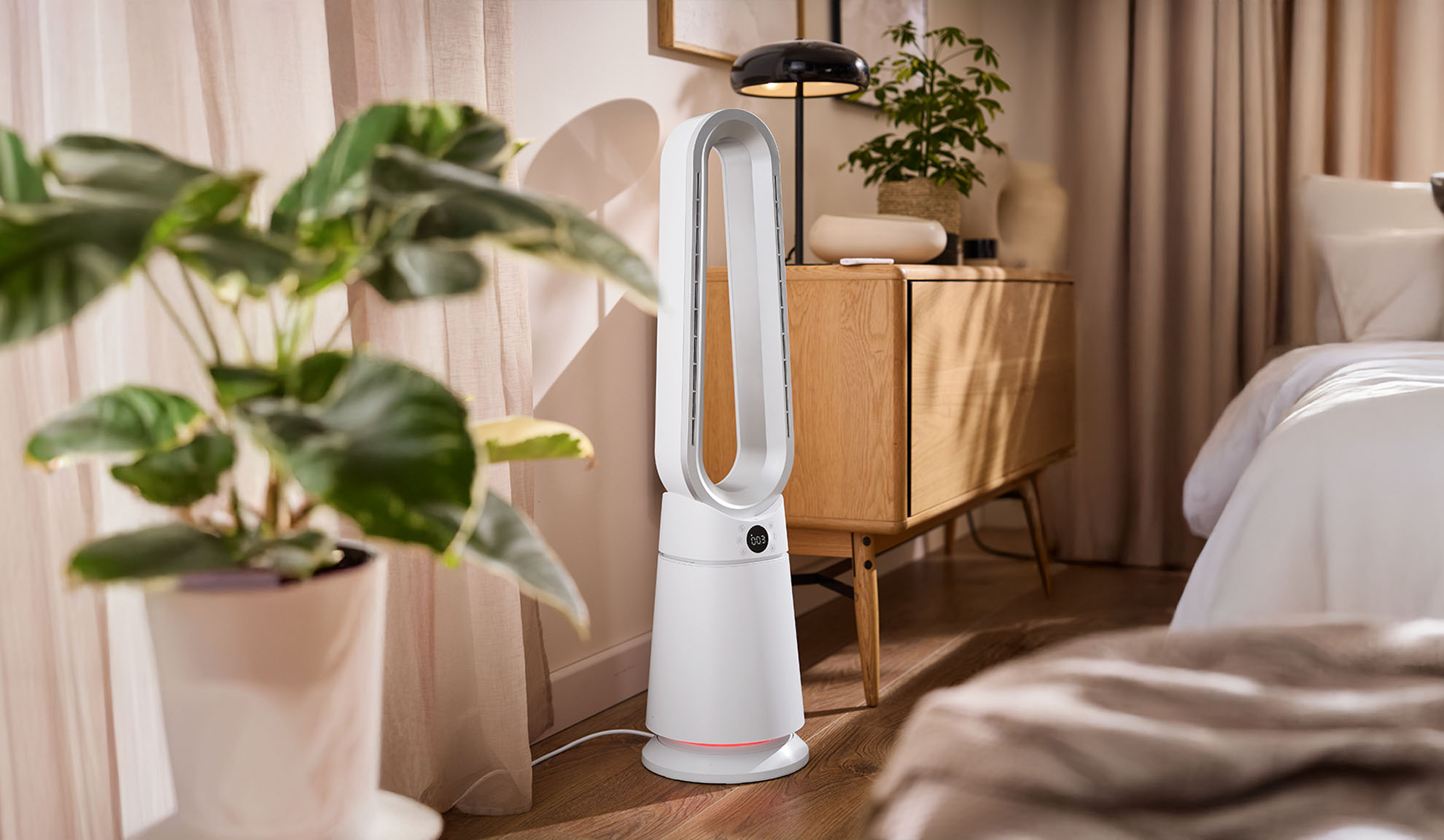 Bílý věžový ventilátor v moderní ložnici s rostlinami a dřevěným nábytkem.