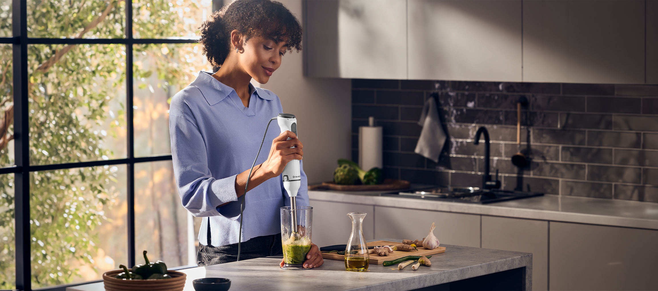 Žena v kuchyni připravuje zelené smoothie ponorným mixérem.