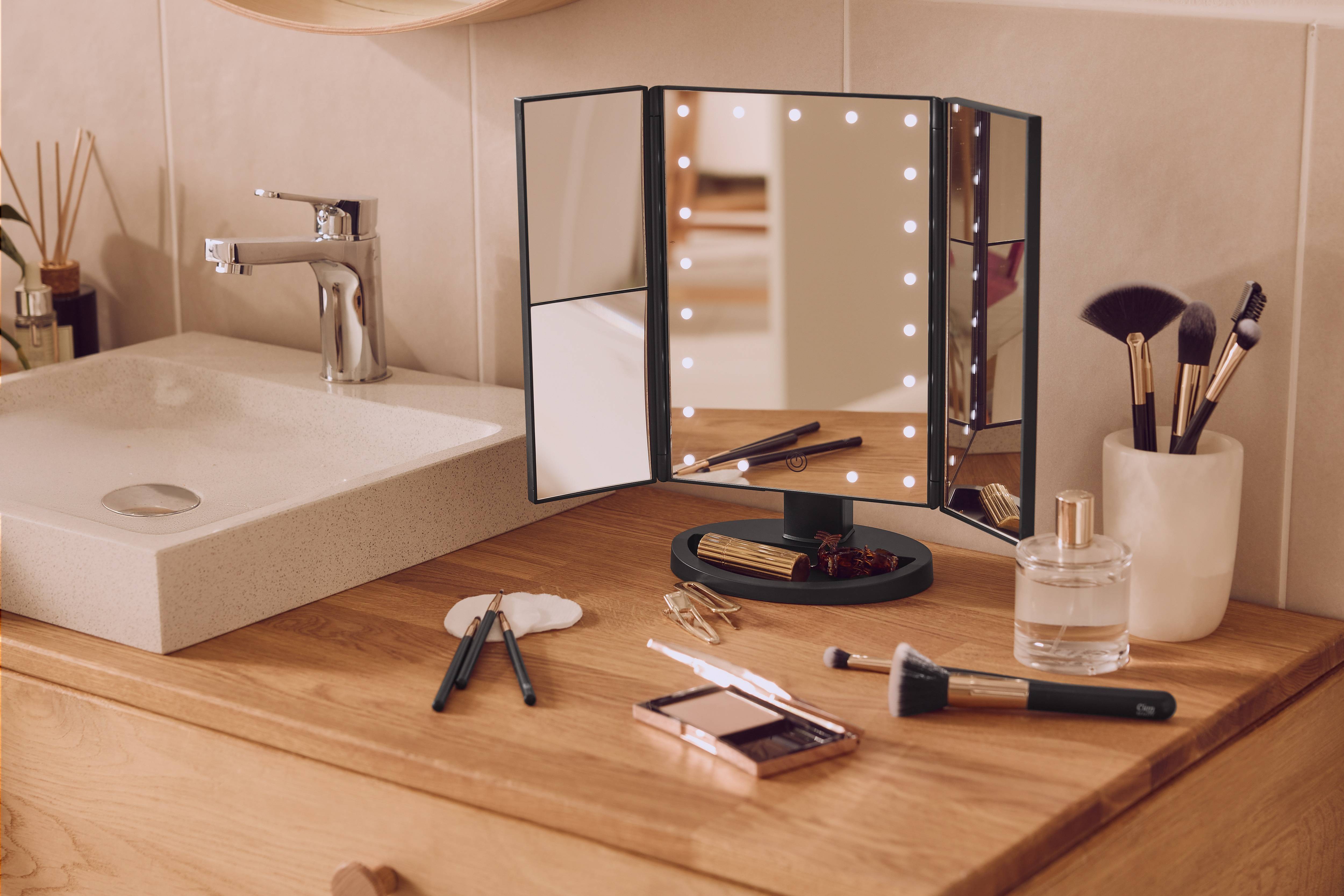 Koupelnová deska s osvětleným kosmetickým zrcadlem, štětci na make-up a kosmetikou.
