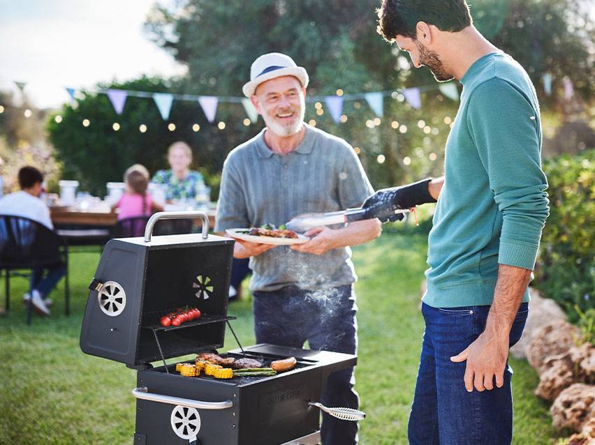 Muži grilují maso a zeleninu na zahradní párty s rodinou.