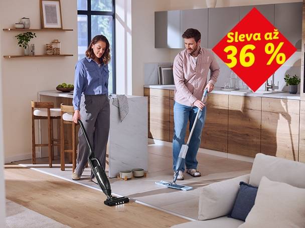 Muž a žena uklízejí kuchyň a obývací pokoj, žena používá tyčový vysavač, muž mopuje. Sleva až 36 %.