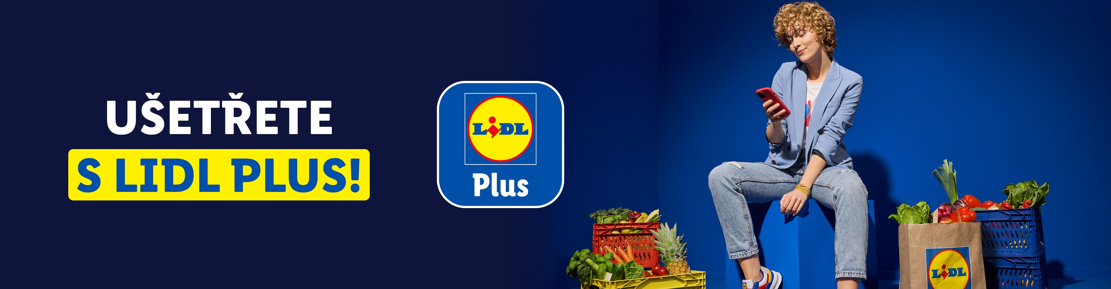 Žena sedící na modré kostce s telefonem, obklopená bednami a taškou s potravinami Lidl.