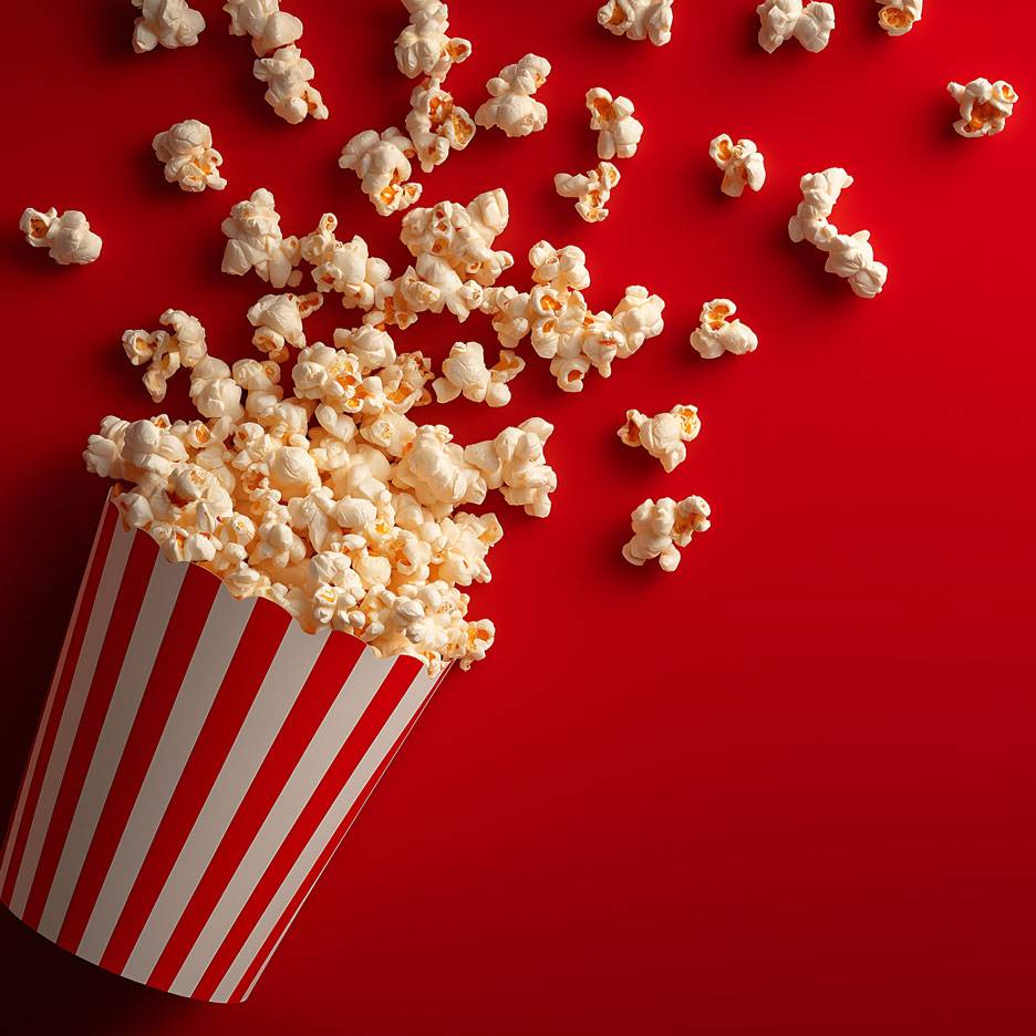 Popcorn na červeném pozadí, část popcornu v pruhovaném papírovém kelímku.
