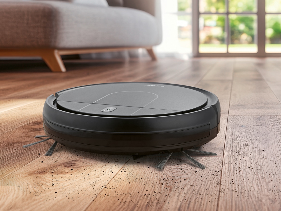Černý robotický vysavač uklízí nečistoty na dřevěné podlaze.
