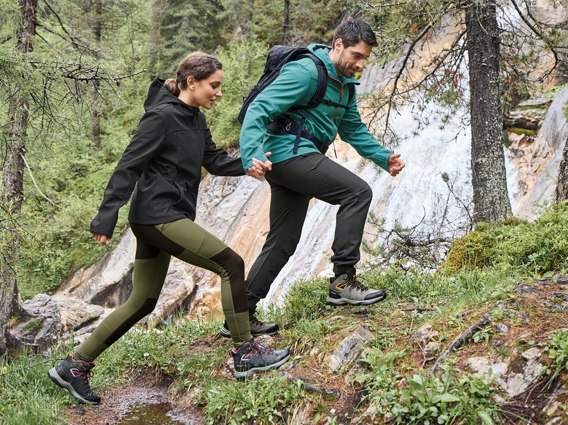 Muž a žena v outdoorovém oblečení a turistické obuvi stoupají do kopce u vodopádu.