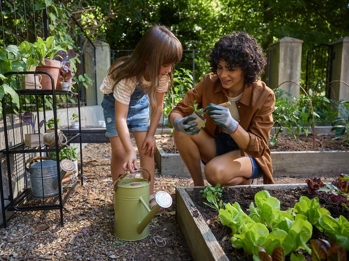 Žena a dítě s konví a rostlinami v zahradě.