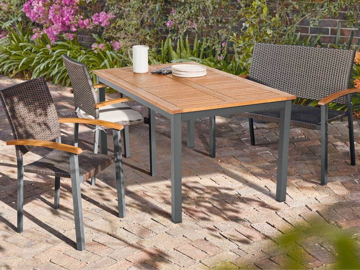 Venkovní jídelní sestava s dřevěným stolem a čtyřmi židlemi na cihlové terase.
