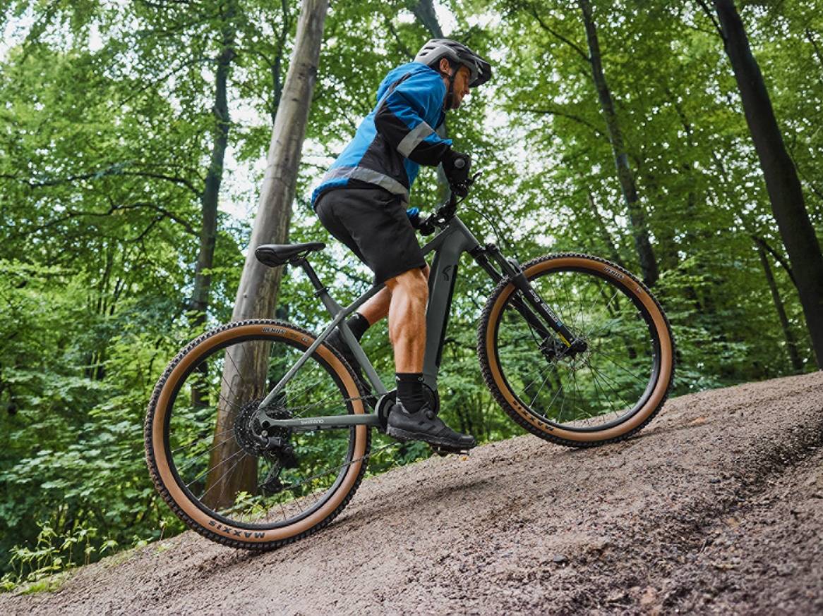 Muž na horském elektrokole stoupá do kopce v lese.