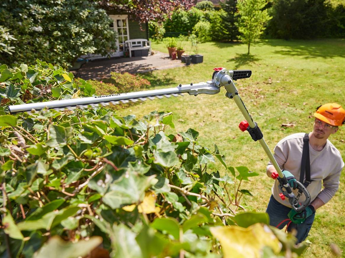 Muž stříhá živý plot pomocí nůžek na živý plot s dlouhou rukojetí.