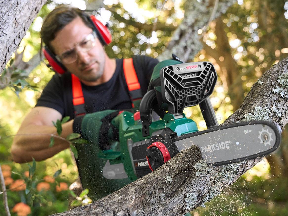 Muž s ochrannými brýlemi a sluchátky řeže větev motorovou pilou.