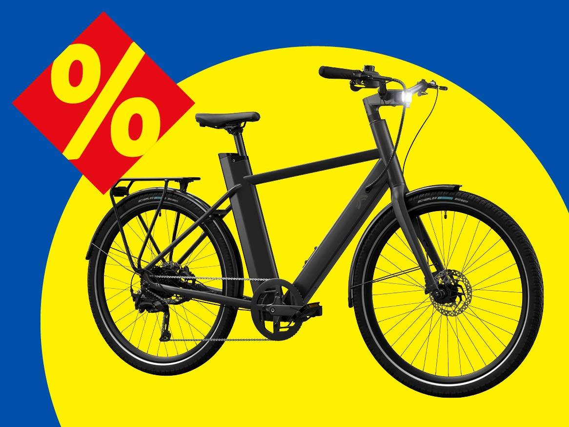 Černé elektrokolo s nosičem a předním světlem na žlutém pozadí s červeným symbolem procent.