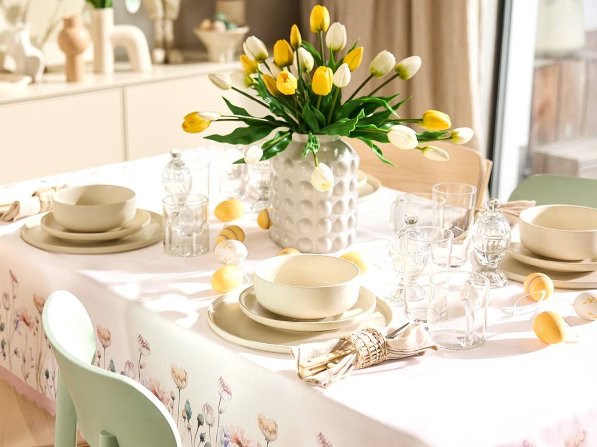 Velikonoční stůl s vázou žlutých a bílých tulipánů, nádobím a dekorativními vajíčky.